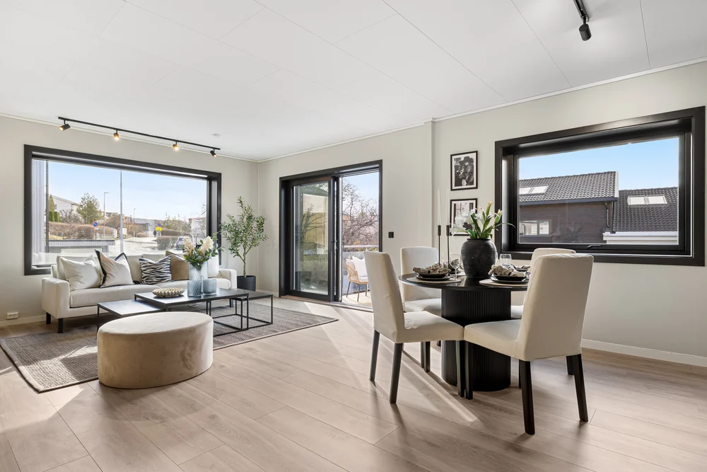 Spiseplass og stue med sorte vinduskarmer og lyse møbler.