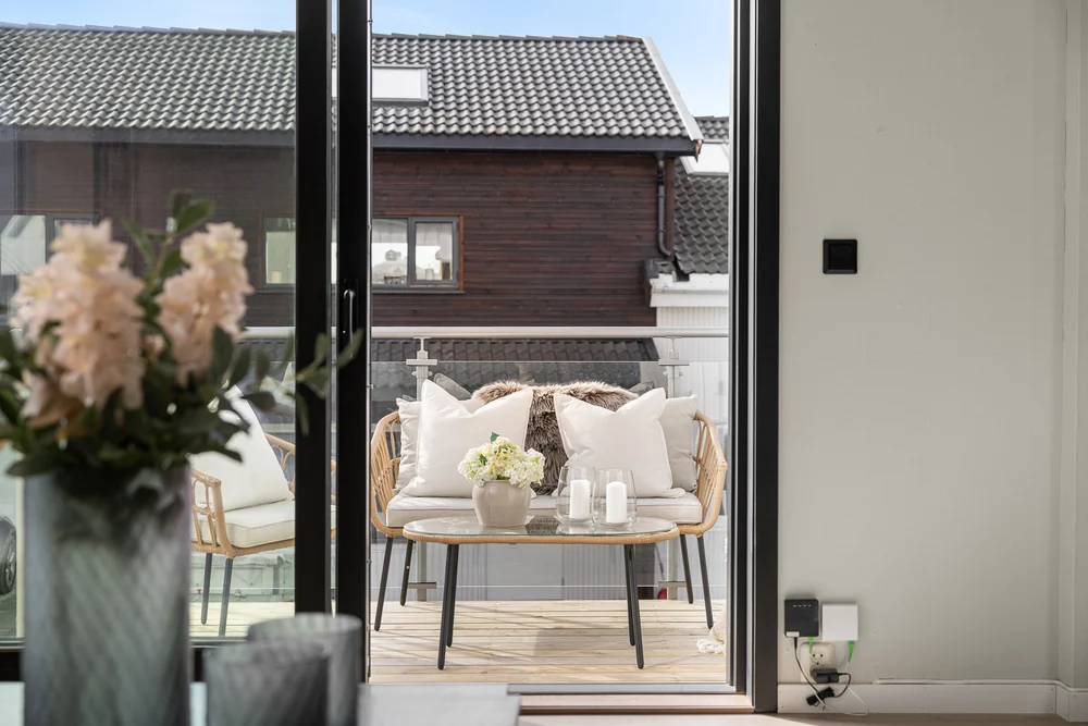 Stylet terrasse med lyse stoler og blomster, sett gjennom terrassedøren.