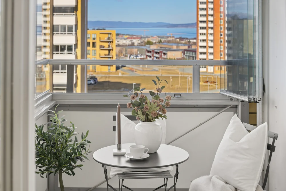 Innglasset balkong med kafébord, lyse stoler og utsikt over byen.